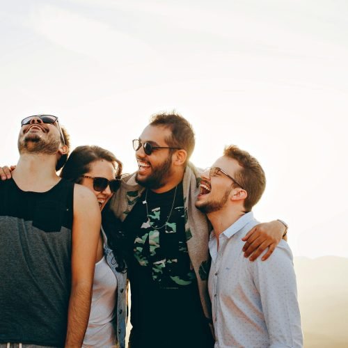 A group of young adults laughing and enjoying time together outdoors under the sun.